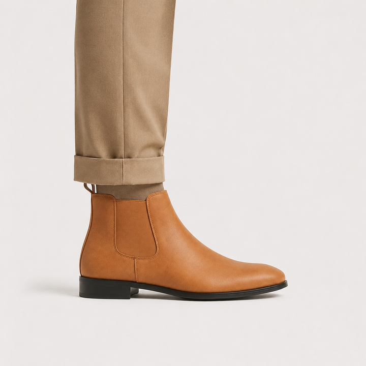 A tan leather Chelsea boot worn with cuffed khaki trousers, shown from a side profile against a light gray studio background.