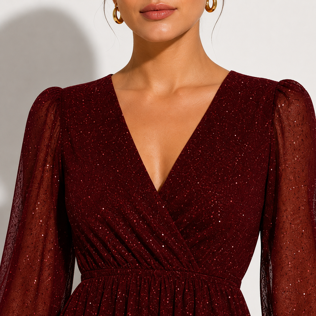 A close-up of a model wearing a deep burgundy sparkly wrap dress with sheer long puff sleeves and a deep V-neckline.
