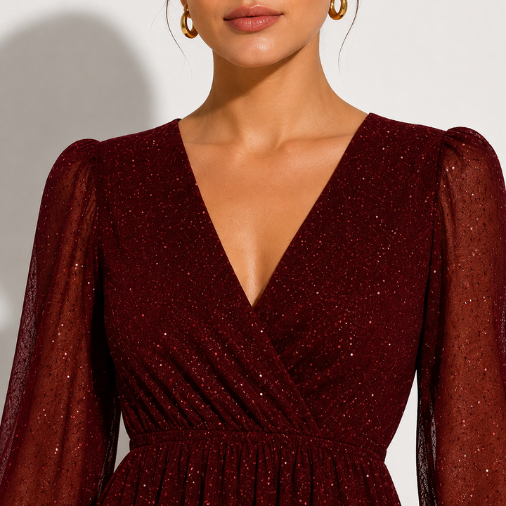A close-up of a model wearing a deep burgundy sparkly wrap dress with sheer long puff sleeves and a deep V-neckline.